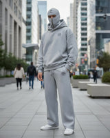 a men stand on a dubai street and looking front in camera and wear ninja hoodie co-ord set with attach mask and white shoes.