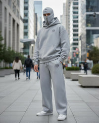 a men stand on a dubai street and looking front in camera and wear ninja hoodie co-ord set with attach mask and white shoes.