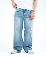 Man wearing light wash baggy wide-leg jeans with a white t-shirt and white sneakers, showing a relaxed 90s-inspired denim style